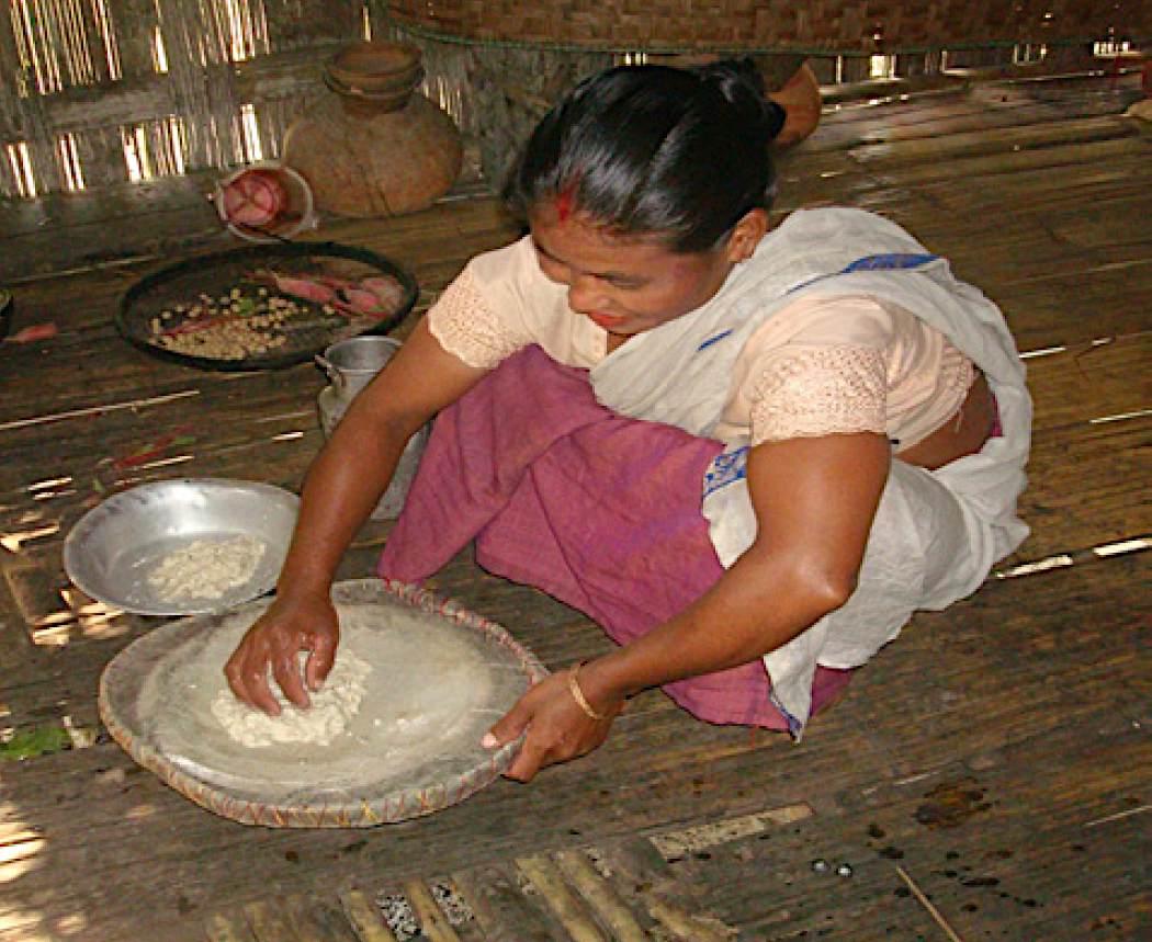 India, Assam. Mishing woman filtering a fermented mash to get apong beer